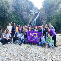 Group posing in nature with the WCU flag