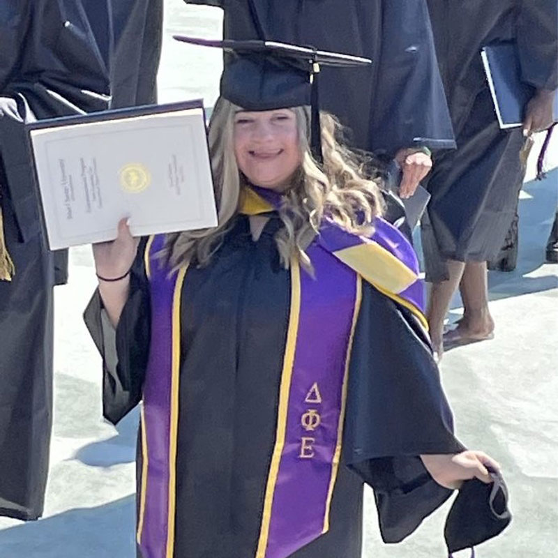 A woman at Commencement holding her diploma up with one hand.