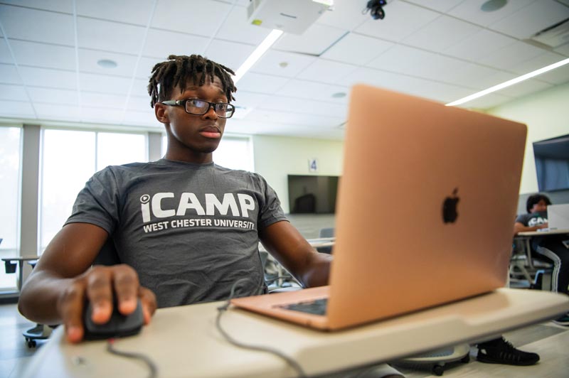 student wearing iCamp tshirt while working on a laptop