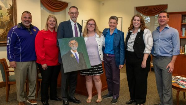 Katie Lickfield and West Chester University administrators gather during a surprise meeting to present a portrait of WCU President Chris Fiorentino. Pictured (L to R) standing are Vice President for University Affairs and Chief of Staff Andrew Lehman; Director of Autism Services/Dub-C Autism Program (D-CAP) Cherie Fishbaugh; WCU President Chris Fiorentino; artist and WCU alumna Katie Lickfield; Dean of the College of Arts and Humanities Jen Bacon; Vice President for Student Affairs Tabetha Adkins; and Executive Vice President & Provost Jeffery Osgood.