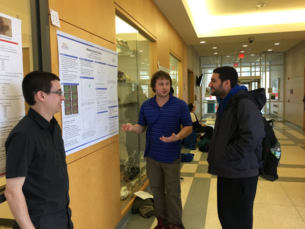 Ben Plumridge, a graduate student working with Dr. Andreas Aristotelous, explaining the topic of his poster to another student.